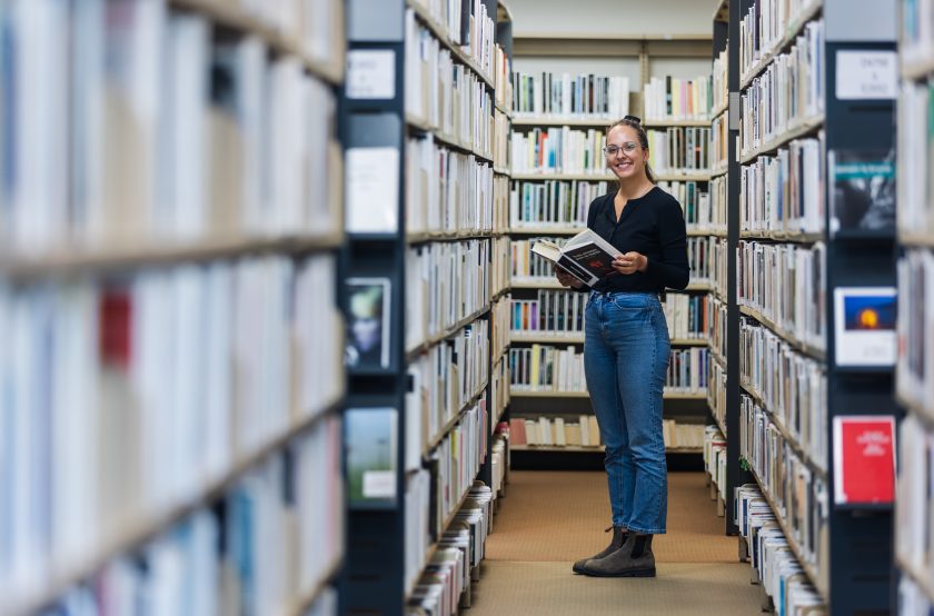 Femme dans une allée de la bibliothèque avec un livre dans les mains