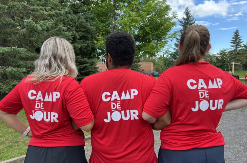 Trois animateurs de camp de jour de dos qui montrent leurs chandails.
