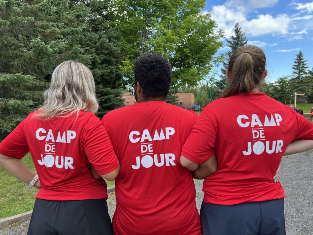 Trois animateurs de camp de jour de dos qui montrent leurs chandails. 